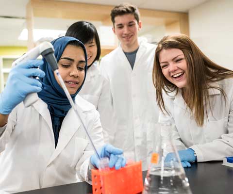 Trois jeunes chercheuses et un jeune chercheur rient et travaillent dans un laboratoire.