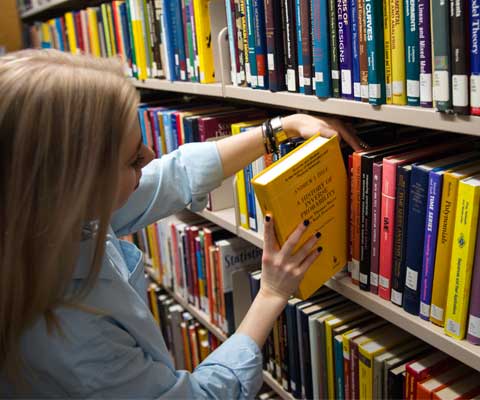 Une jeune femme place un livre sur les rayons dans la bibliothèque.