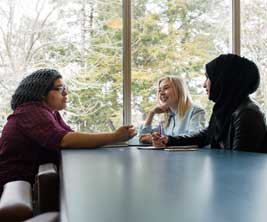3 female students sitting on table discussing with each other
