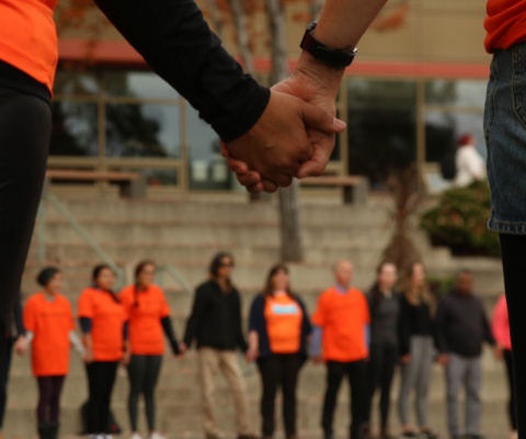People dressed in orange shirts, holding hands in a circle