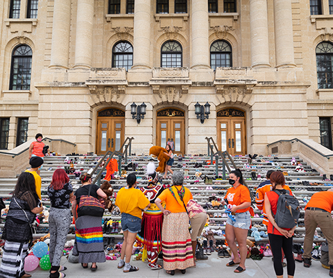 People wearing orange and traditional Indigenous clothing looking at the building
