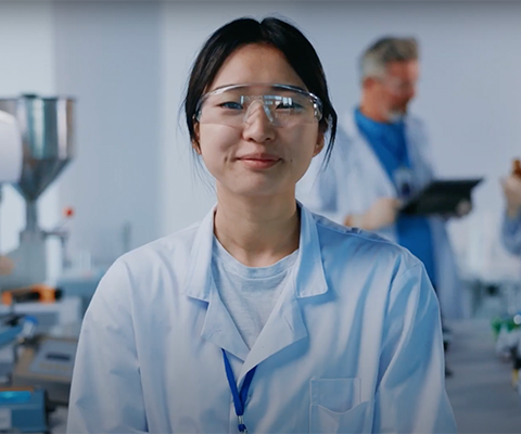 Woman looking at the camera, wearing a lab coat and safety goggles