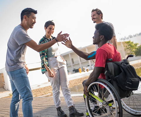 Four young people, one in a wheelchair, smiling and giving high-fives.