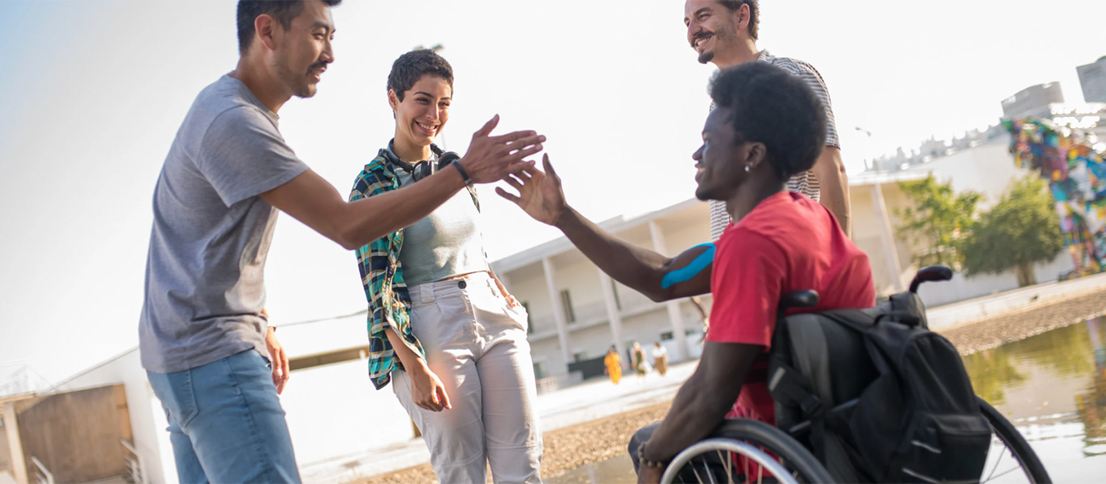 Four young people, one in a wheelchair, smiling and giving high-fives.