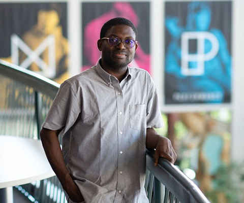 Photo of Taiwo Afolabi in a button-up shirt, leaning on a railing