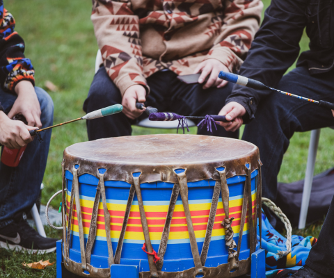 Three people around a drum holding drumsticks.