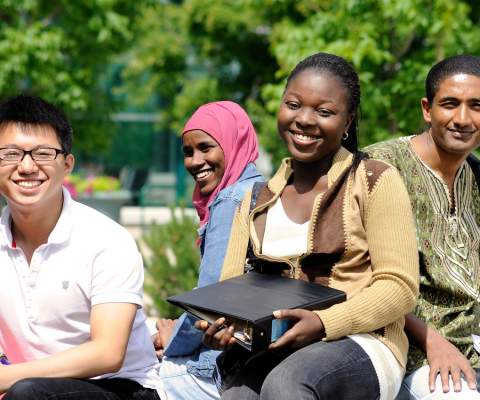A group of four students sitting outside, smiling.